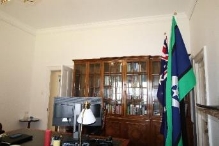 A picture of the Prime Minister's study room at Kirribilli House with Australia's main flags, dark wood furniture, a monitor and lamp in the room