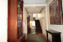 A picture of a Kirribilli House hallway showing art on the white walls and dark wood stained stairs and cabinets through the hallway