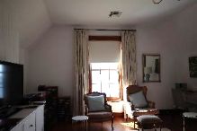 A picture of a Kirribilli House family room with a television, brown chairs with blue cushions and an opened window allowing light through the room
