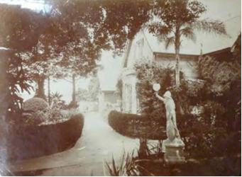 A sepia tone image of the Kirribilli House main entry pathway with trimmed hedges, trees and a small statue