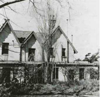 A black and white picture of Kirribilli House with leafless trees in front and large bushes on the ground