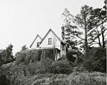 A black and white image of Kirribilli House from slightly below, showing the house's structure and large trees and bushes surrounding its grounds