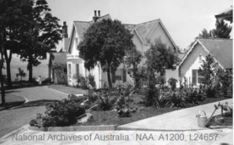 A black and white image of Kirribilli House entry driveway, showing the gardens to the right of the property with small bushes and medium and large trees around the estate 