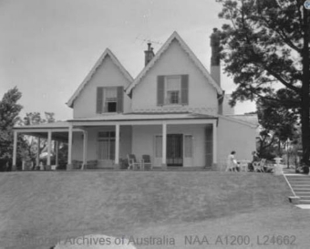 A black and white image of Kirribilli House from slightly below the sloped garden, showing the house's structure, the garden stairs and outdoor furniture on the veranda