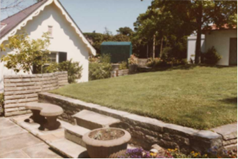 A picture of a raised lawn by Kirribilli House, with two steps and surrounding pot plants and flowers