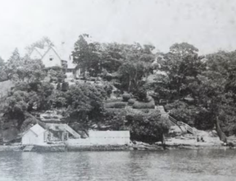 A black and white picture of Kirribilli House from the harbour surrounded by a body of water and the house and its grounds surrounded by vegetation