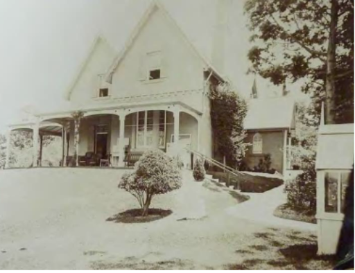 A sepia tone picture from the sloped garden looking up at Kirribilli House with stairs leading up to the property, a path leading to its side access points and a women by a small, singular tree