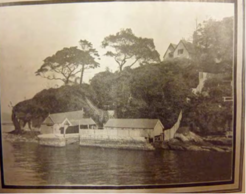 A sepia toned picture of the boat harbour underneath the cliff from Kirribilli House surrounded by large trees and a body of water