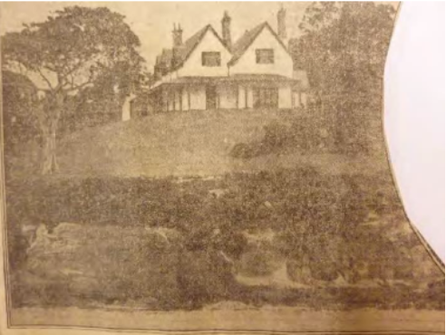 A sepia toned image of Kirribilli House from the harbour overlooking the cliff, trees, the house and its grounds. 