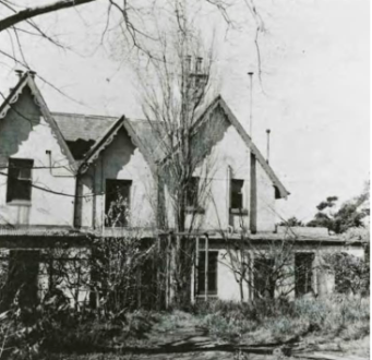 A black and white picture of Kirribilli House with leafless trees and large bushes in front of the property 
