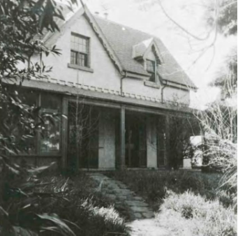 A black and white picture of Kirribilli House from its side showing the gardens and path leading to the house, columns that surround the veranda, and opened windows on the top and bottom floors.
