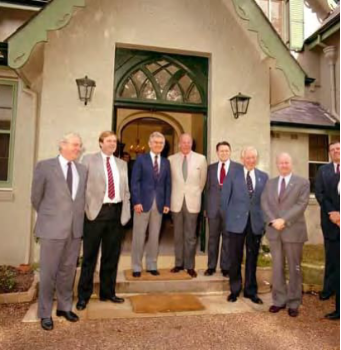A picture of 8 men in suits standing for a picture in front of the Kirribilli House entry way. 